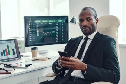 Black trader working in an office, analyzing trading charts on a computer screen.