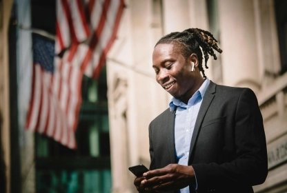Young Black trader on Wall Street looking at his phone.