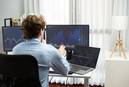 Trader sitting in an office in front of a computer with trading charts on the screen.