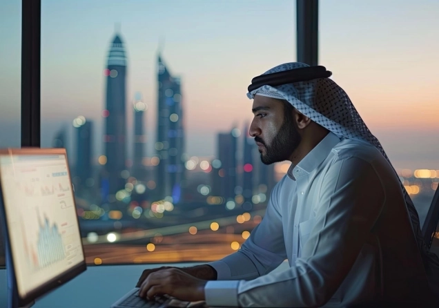 Muslim trader sitting in an office in front of a computer with trading charts on the screen.