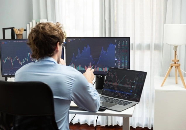 Trader sitting in an office in front of a computer with trading charts on the screen.
