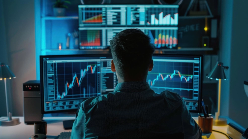 Trader sitting in an office in front of a computer with trading charts on the screen.